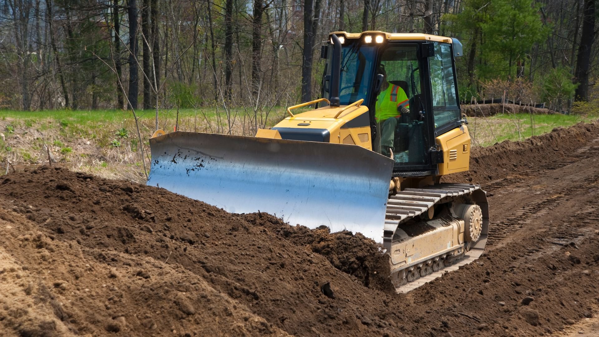 Yellow bulldozer moving dirt in forest clearing during landscaping work