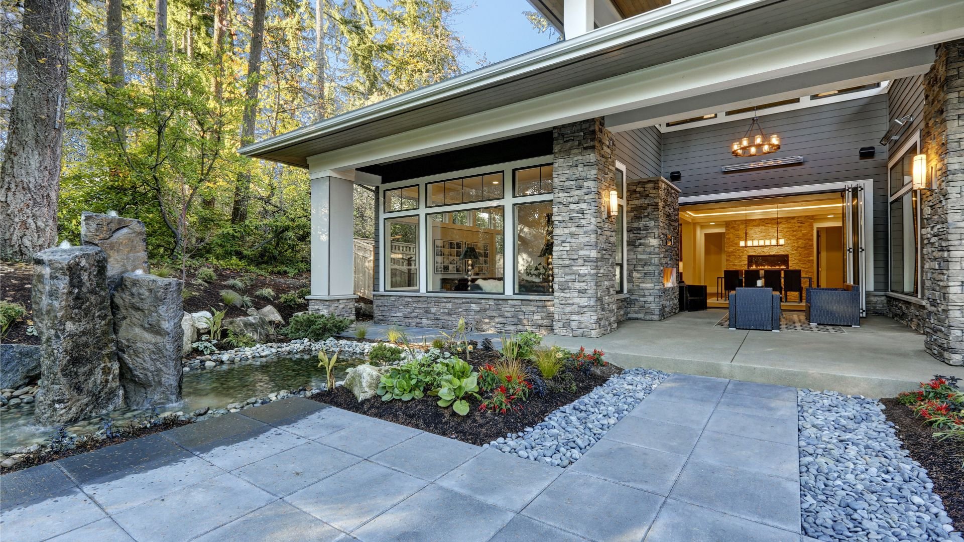 Modern stone house with water feature and landscaped entrance at sunset