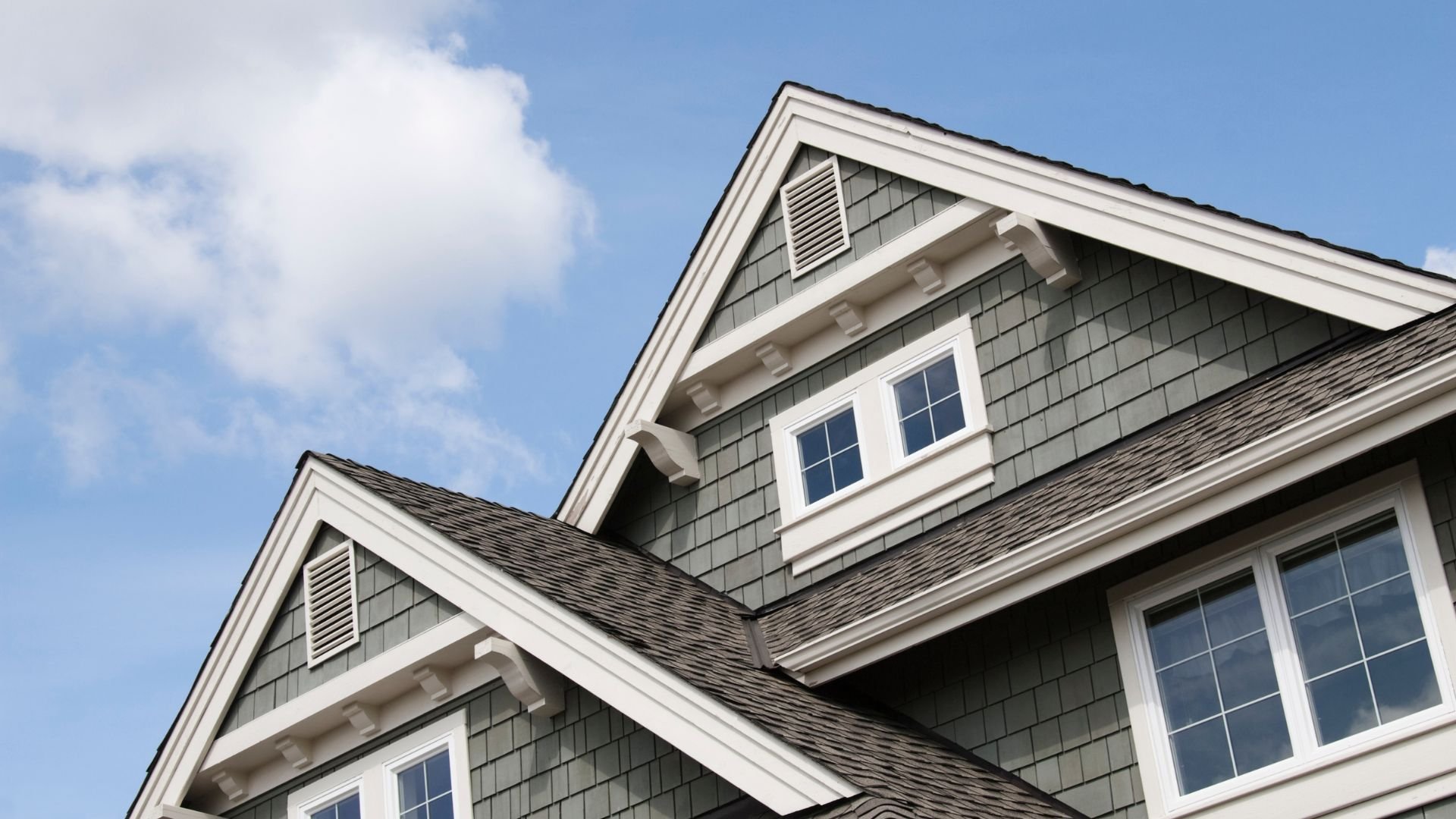 Gray shingled house with white trim against a blue sky
