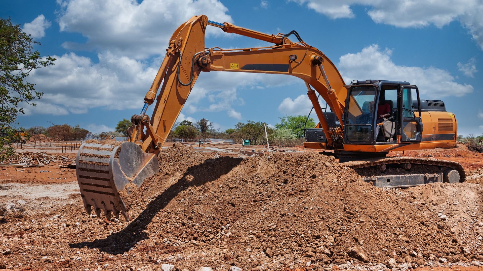 Yellow excavator digging earth at construction site under cloudy sky