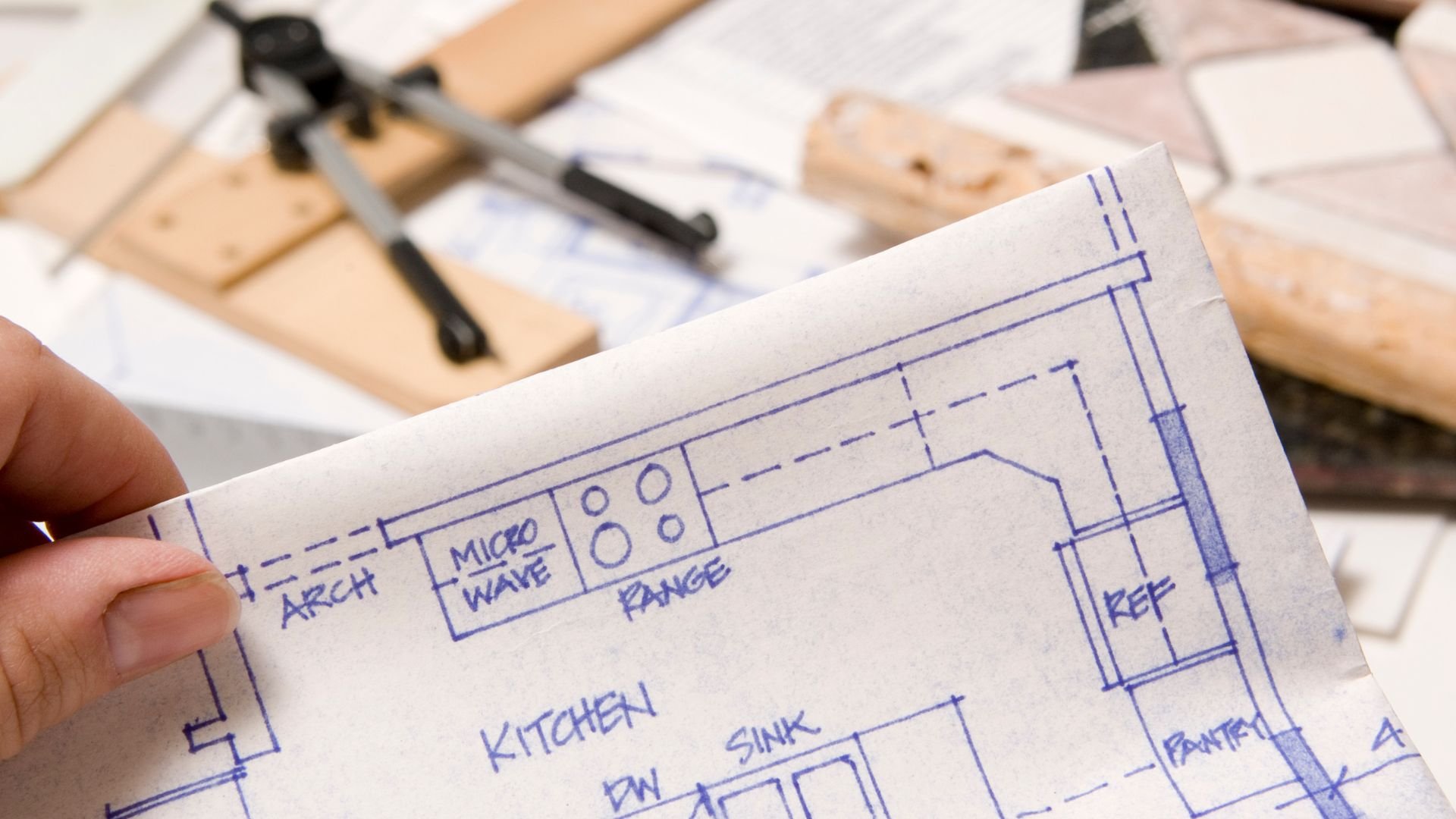 Hand holding kitchen blueprint with microwave, range, and sink layout