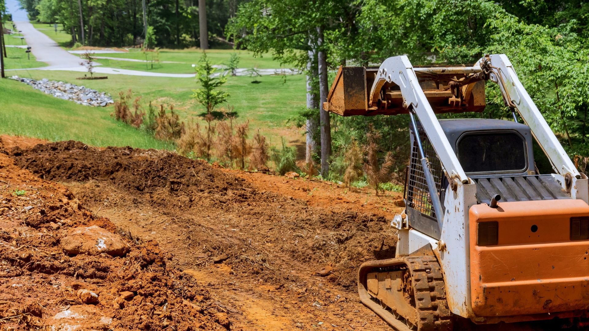 Skid steer loader working on dirt excavation near landscaped green area